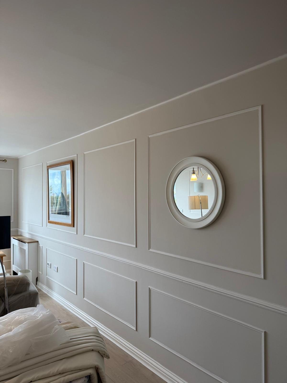 Living room wall finished with white panel moulding, dado rail and a round mirror