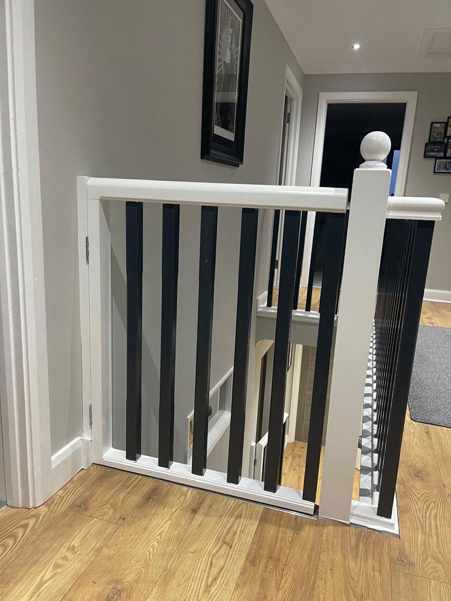 Bespoke white and black stair gate at the top of a landing, matching the banister